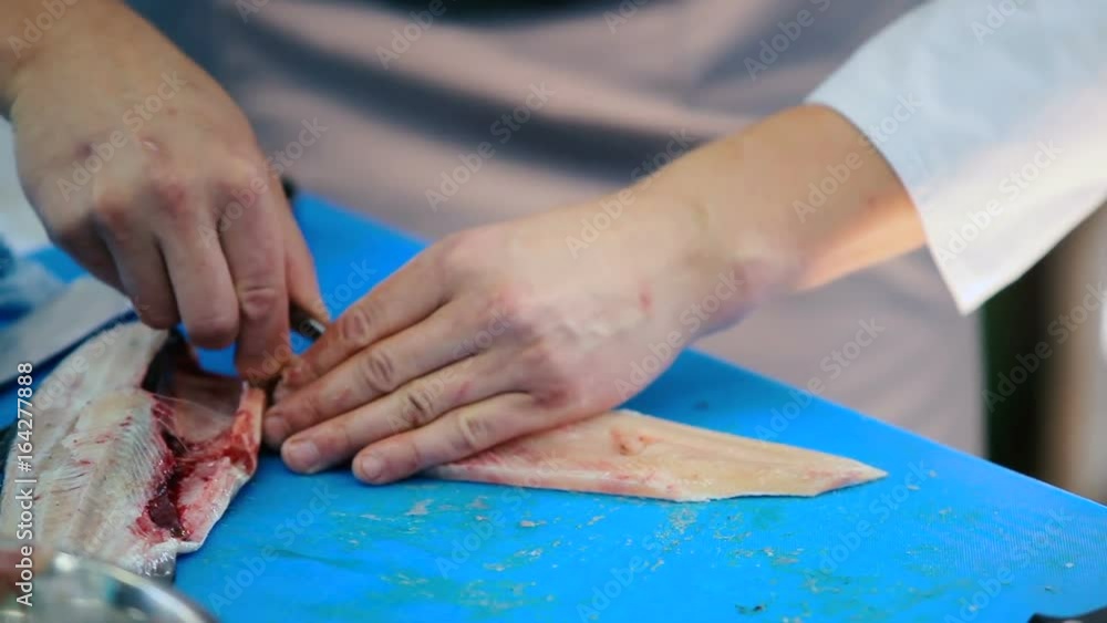 Close-up. The cook preparing the fish on the kitchen of the restaurant. A man cleans the fish fillets from the bones. Man pulls out the bones from fish fillets with tweezers. Close-up. The cook preparing the fish on the kitchen of the restaurant. A man cleans the fish fillets from the bones. Man pulls out the bones from fish fillets with tweezers.