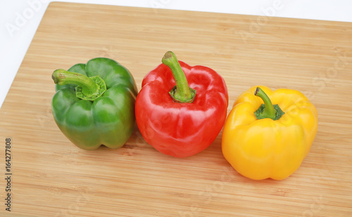 Green, red and yellow bell pepper on wood background.