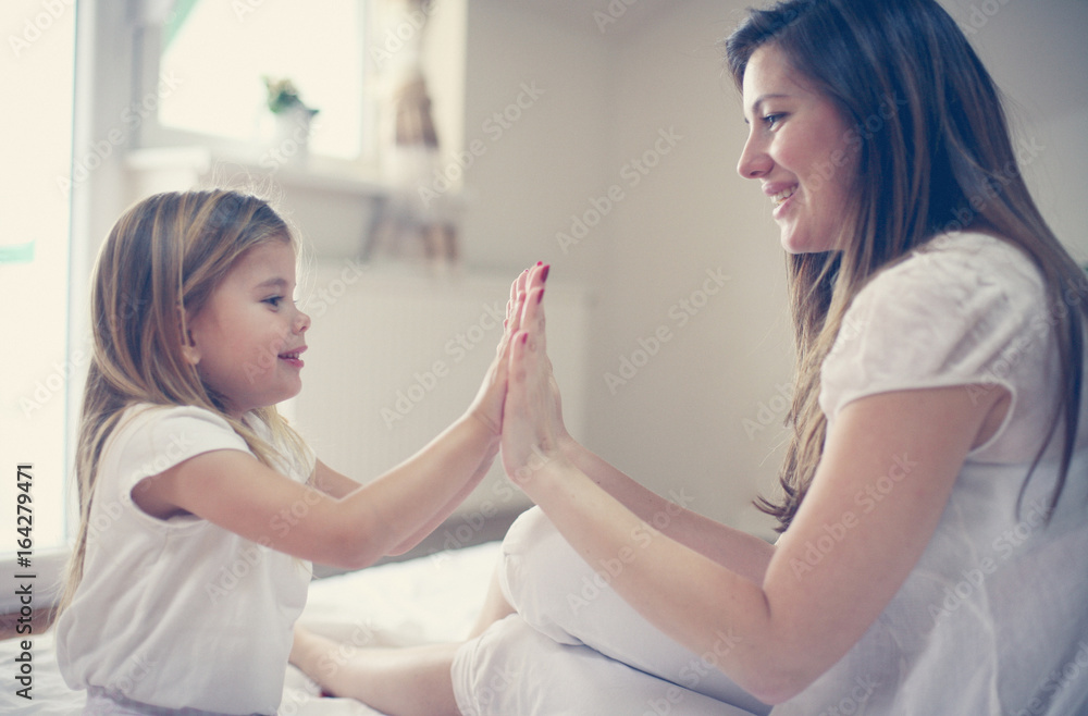 Mother with her cute little daughter sitting on bed.