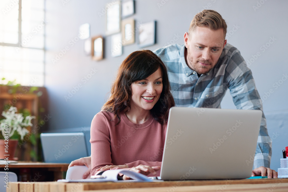 Smiling coworkers using a laptop together in an office Smiling coworkers using a laptop together in an office