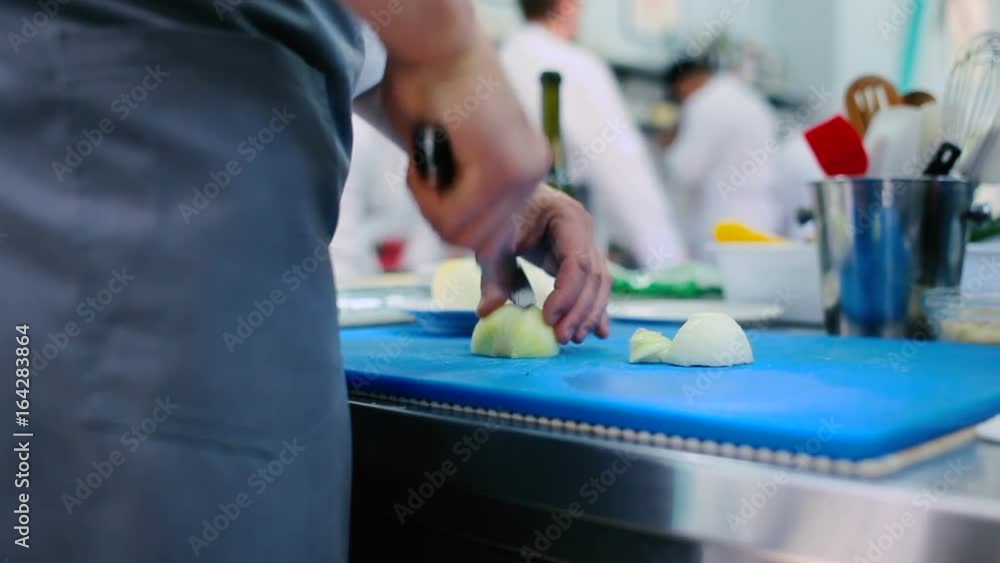 The cook cutting three onions on the board with knife. The cook cutting three onions on the board with knife.