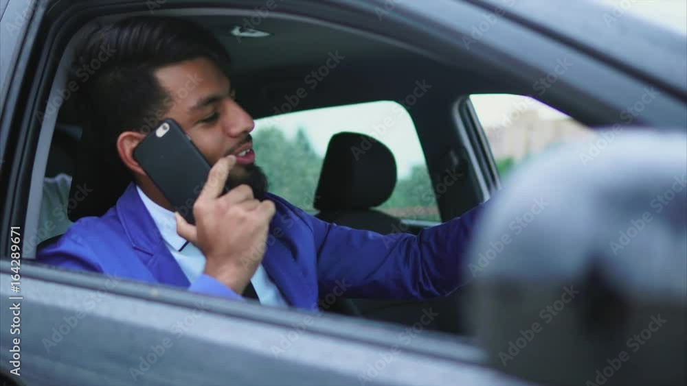 Modern arab man in formal wear sitting in right-hand drive car on the driver's seat and talking on cell phone Modern arab man in formal wear sitting in right-hand drive car on the driver's seat and talking on cell phone