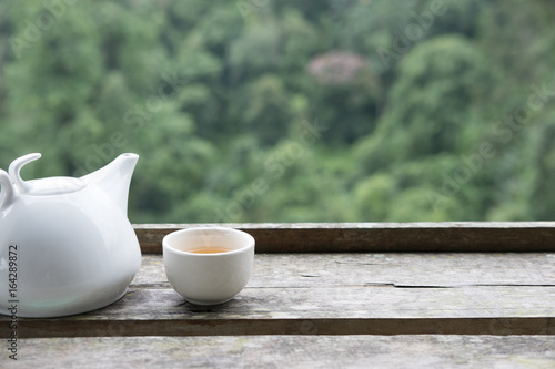 white tea in cup and mug on wood table with green nature background