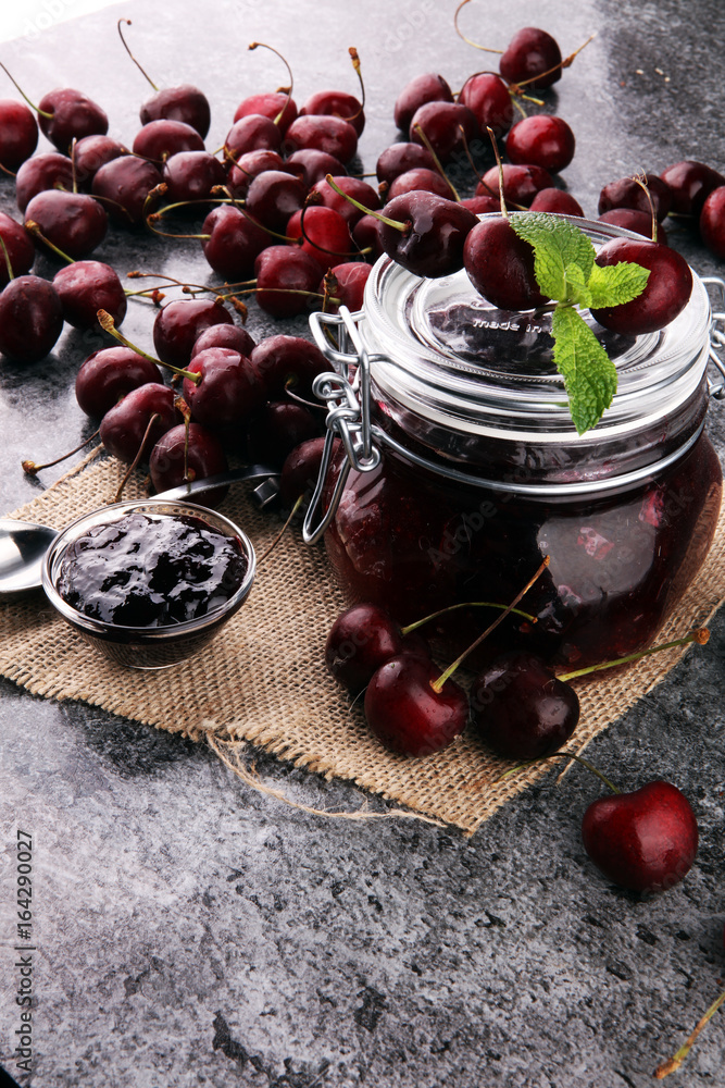 Jar of cherry jam, sour cherries and spoon on grey vintage backg