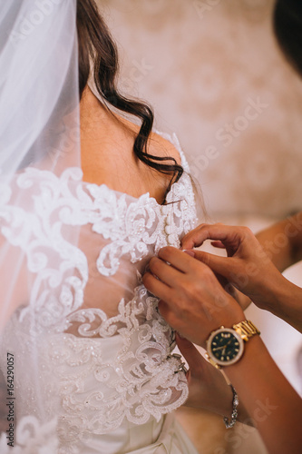 stylish happy bride putting on earrings and smiling, rustic wedding morning preparation in home. bridal getting ready. emotional moment. space for text