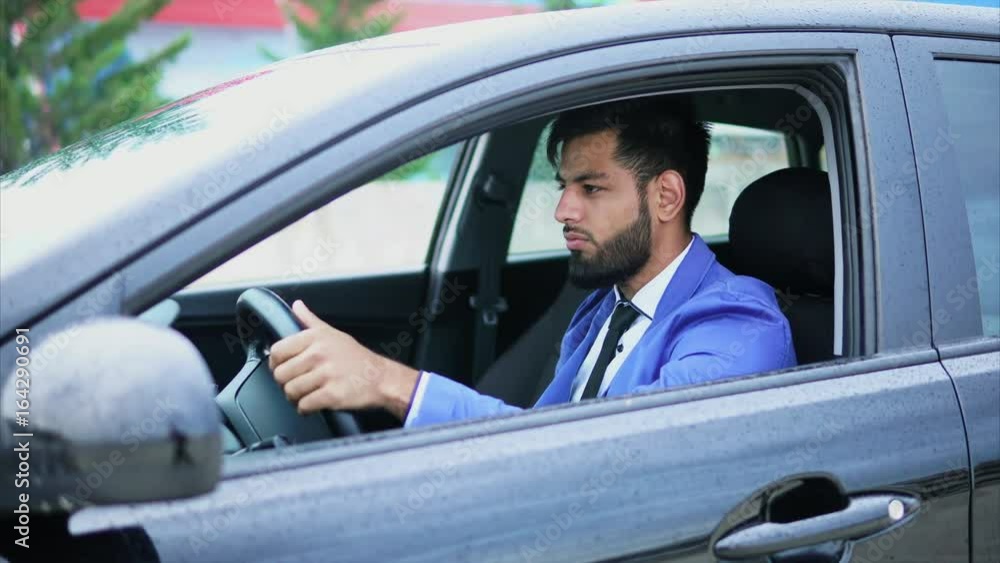 Man in suit driving the car. Muslim man with serious face driving left-hand car in rainy weather. Man in suit driving the car. Muslim man with serious face driving left-hand car in rainy weather.
