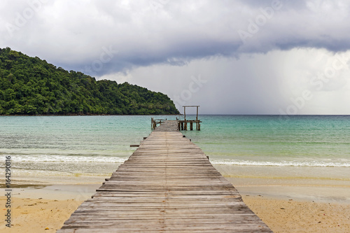 Wooden bridge extended into the sea with views of the tropical islands and the rain clouds coming.