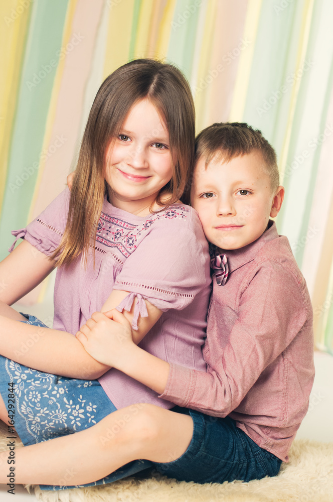 Siblings in a studi sitting on a floor, brother holding the sister Siblings in a studi sitting on a floor, brother holding the sister