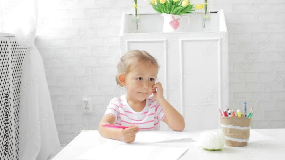 Cute preschool girl sitting by the white table focused on drawing something. Cute preschool girl sitting by the white table focused on drawing something.