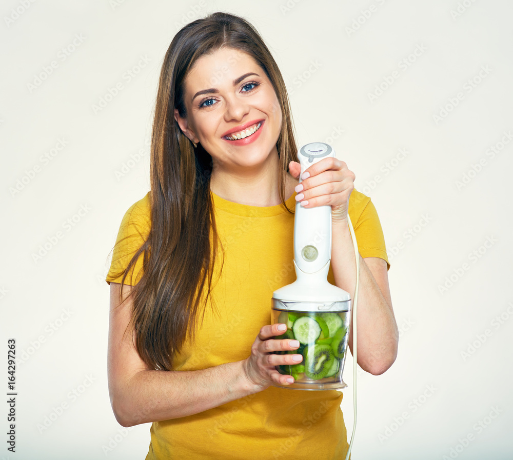 Smiling woman yellow dressed holding blender with green vegetables.