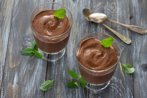 Delicious vegan chocolate mousse with banana, cocoa and mint in glasses on a wooden surface, selective focus