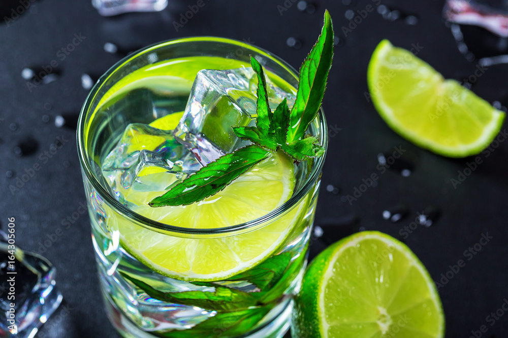 Fototapeta premium Mojito cocktail with lime, ice cubes and mint in highball glass on a black background Copy space