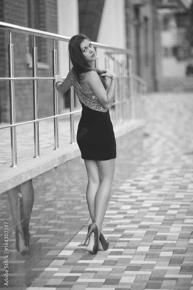 Beautiful sexy girl in short pink black dress on high heels. A young woman  with a beautiful figure and long legs walks around the city. Rear view girl.  Black white photo. foto