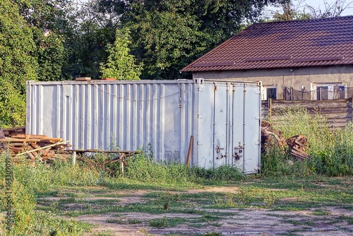 Серый железный контейнер стоит в траве возле дома