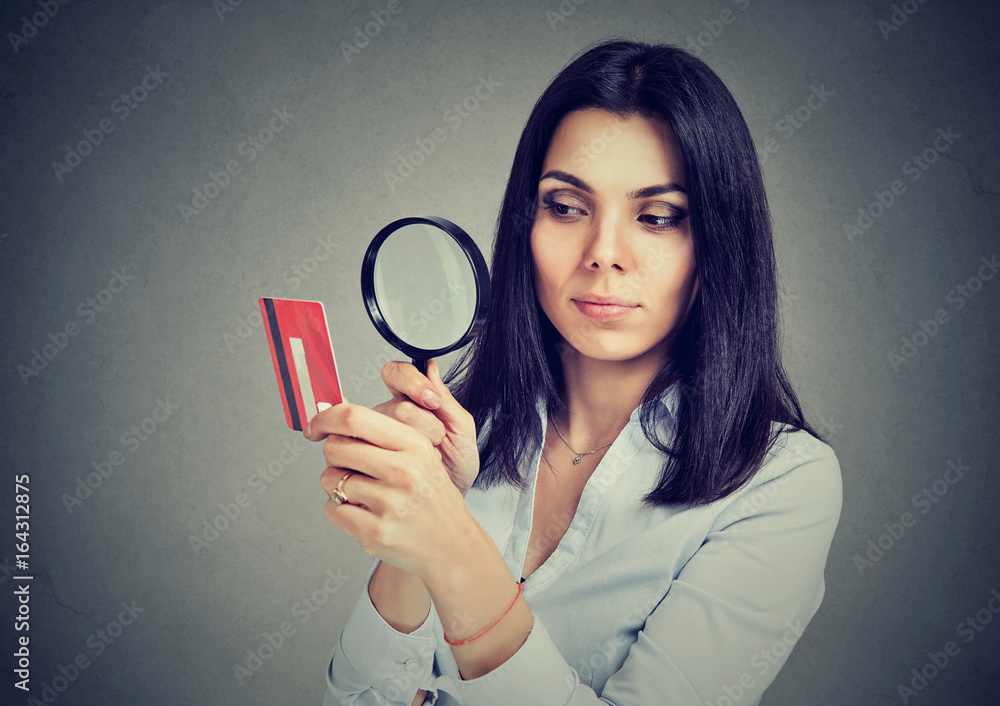 Curious business woman looking at credit card through magnifying glass Curious business woman looking at credit card through magnifying glass
