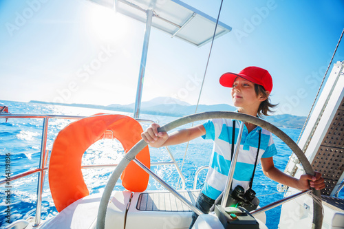Little boy captain on board of sailing yacht on summer cruise. Travel adventure, yachting with child on family vacation. photo