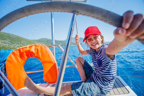 Little boy captain on board of sailing yacht on summer cruise. Travel adventure, yachting with child on family vacation. photo