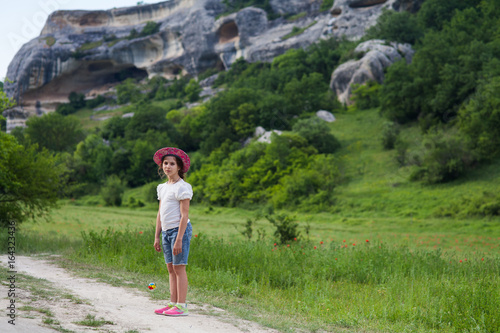 girl in shorts and a hat walking in the summer on a country road with rocks in the background