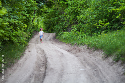 girl in shorts and a hat walking in the summer on a country road