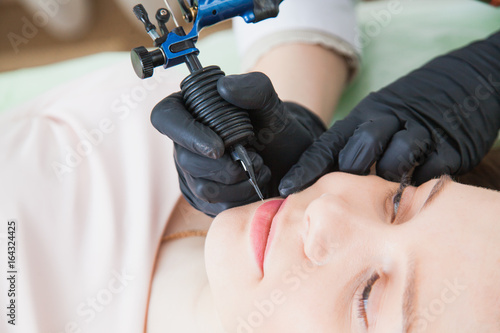 Beautician cosmetologist applying permanent makeup on girl's face.