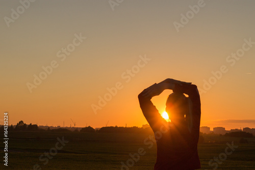 Rear view silhouette of young female standing with hands behind head and looking at sunset