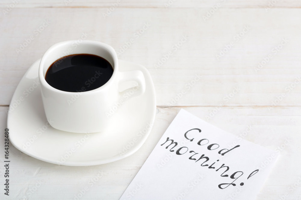 A cup of coffee with message 'good morning' on white wooden table A cup of coffee with message 'good morning' on white wooden table
