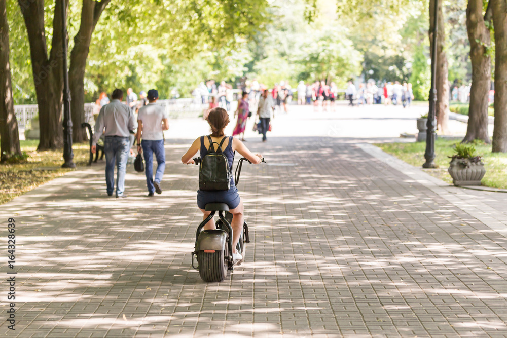 A young woman riding zero-emission eco electric scooter bike in a city park. A young woman riding zero-emission eco electric scooter bike in a city park.