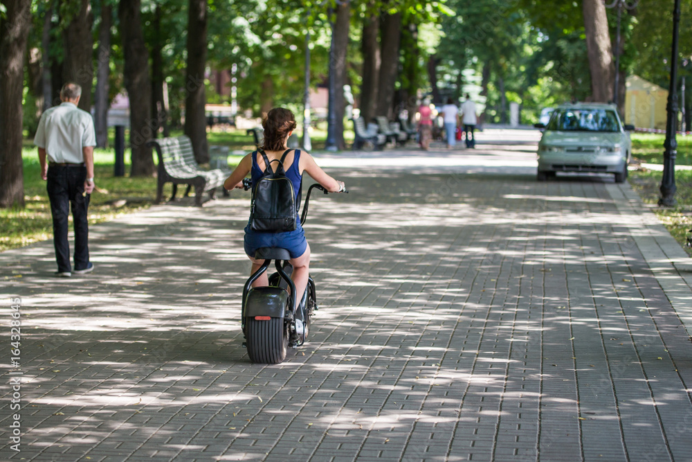 A young woman riding zero-emission eco electric scooter bike  in a city park.