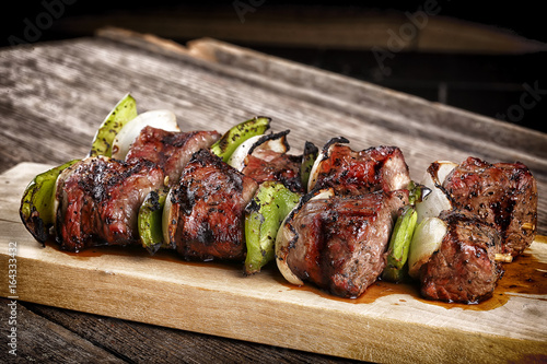 Cooked beef kebabs with vegetables and spices on wooden board 