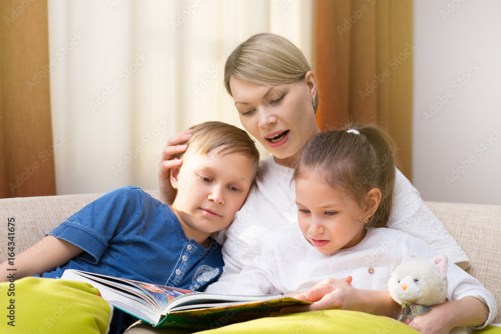 Beautiful mother is reading a book to her young children. Sister and brother is listening to a story. Happy loving family. Beautiful mother is reading a book to her young children. Sister and brother is listening to a story. Happy loving family.