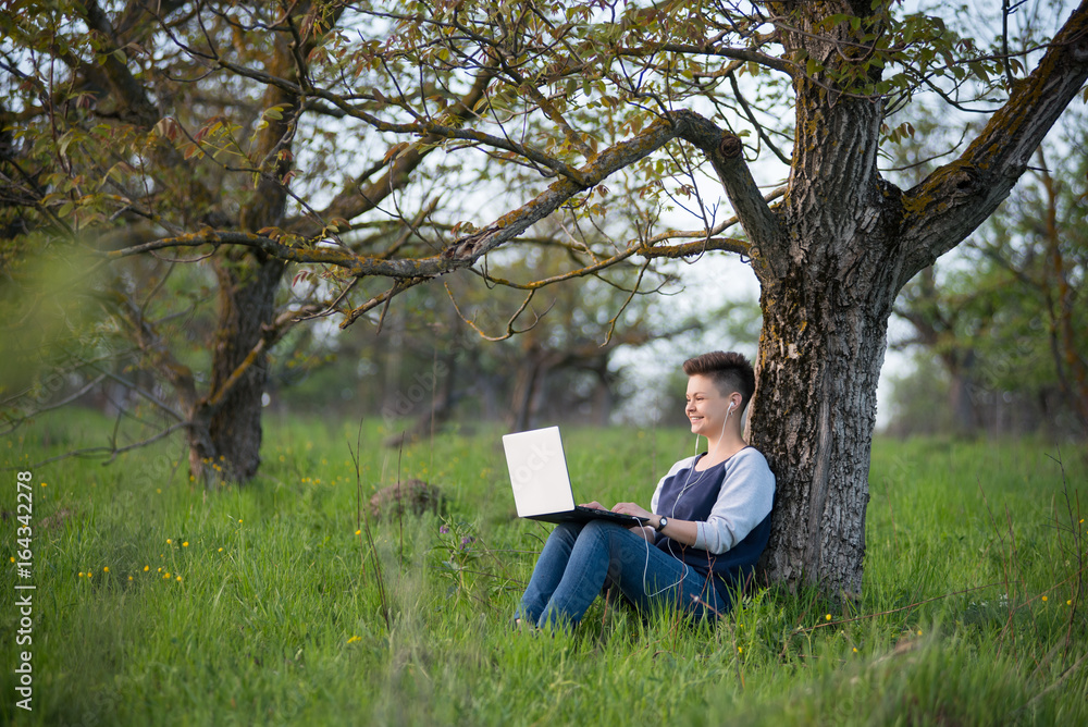 Young smiling woman sitting under the tree in the park using her laptop positivity working studying education relaxation weekend internet online Young smiling woman sitting under the tree in the park using her laptop positivity working studying education relaxation weekend internet online