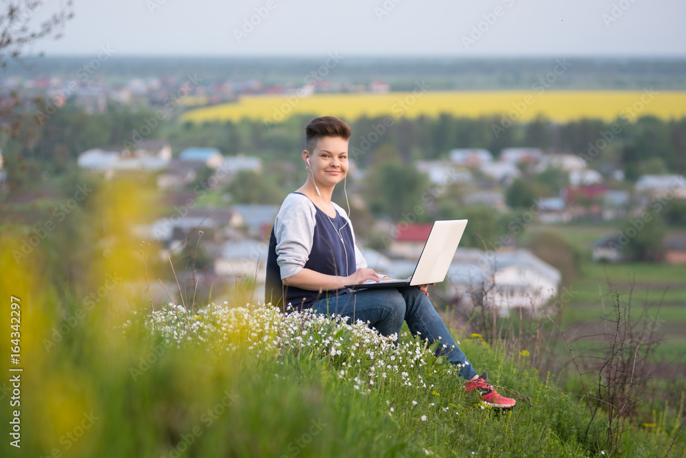 Full length shot of a young woman sitting on top of a hill working on her laptop smiling to the camera joyfully nature hiker travelling tourism online internet 3g 4g mobility connection Full length shot of a young woman sitting on top of a hill working on her laptop smiling to the camera joyfully nature hiker travelling tourism online internet 3g 4g mobility connection