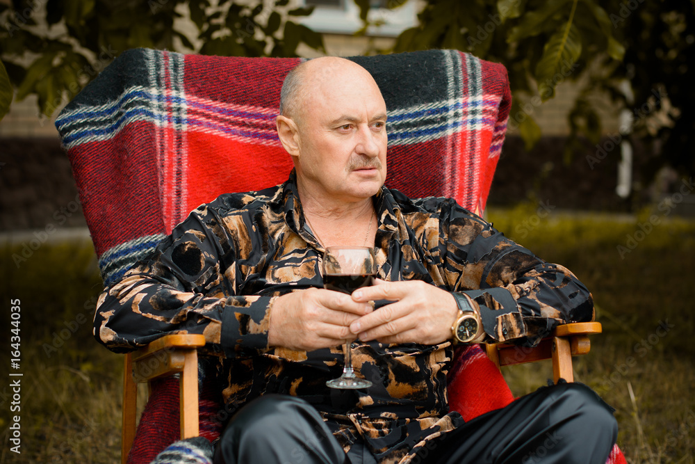 Fototapeta premium Mature stylish man tasting a glass of red wine, traditional red plaid at autumn . Alone seniors smelling a glass of red wine. Thinking about life and problems with wine