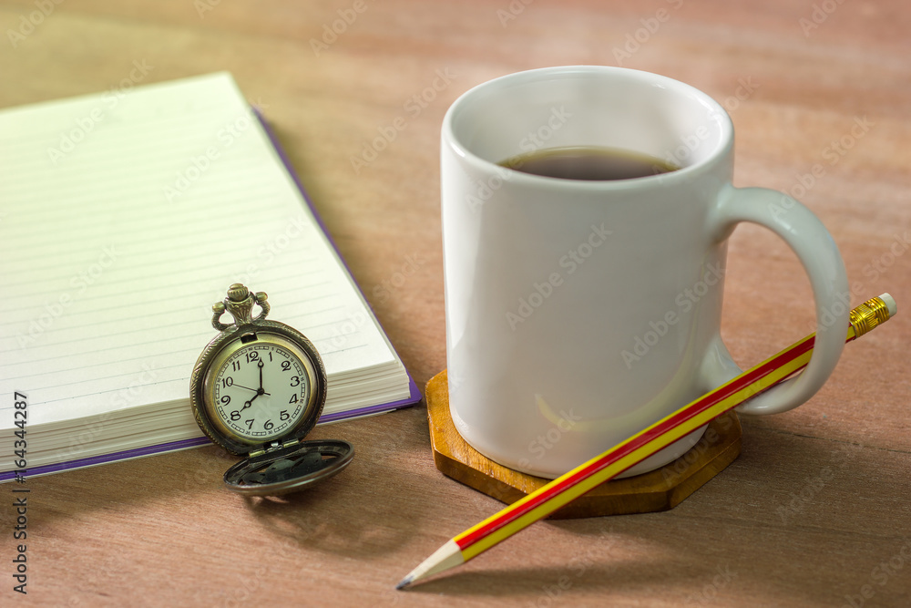 Black coffee with a notebook on a brown table. In the morning and Vintage clock at 8 o’clock. Black coffee with a notebook on a brown table. In the morning and Vintage clock at 8 o’clock.
