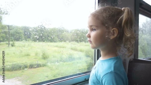 Wallpaper Mural Train departs from station. Little curious girl looking out of window in train. Drops of rain on glass. It's raining outside, child reflecting in glass. Sad child looks out the window. Torontodigital.ca