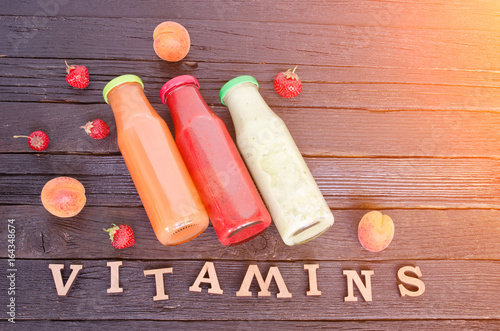 Three bottles with juice, fruit and inscription vitamins on a wooden background, food concept