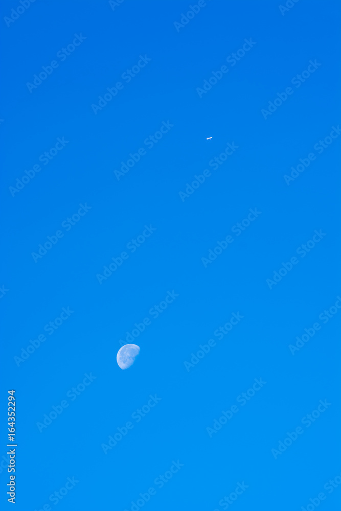 Airplane flying high on a clear sky passing over the moon Airplane flying high on a clear sky passing over the moon