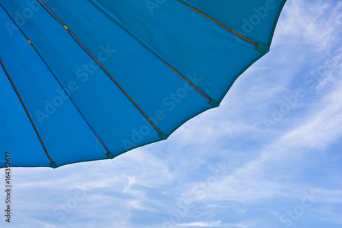 Fragment of a blue garden umbrella against the sky withclouds.