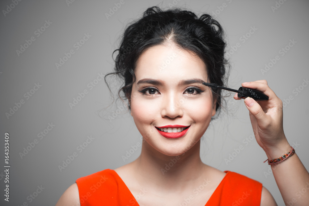 Close-up portrait of beautiful girl touching black mascara to her lashes Close-up portrait of beautiful girl touching black mascara to her lashes