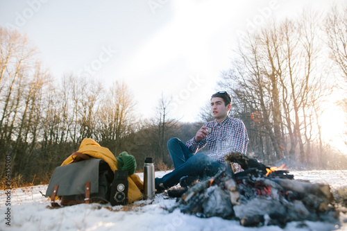 Handsome caucasian scout man warming his hands from bonfire in the winter in mountains. photo