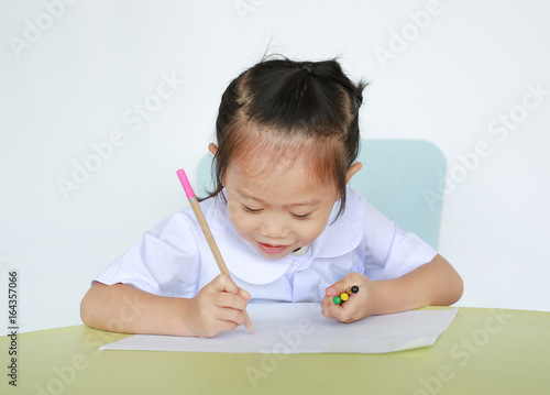 Asian child in school uniform with pencil writing on table isolated on white background. photo