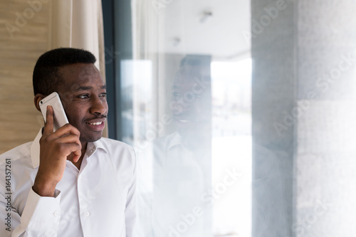 Young businessman checking his phone on an office. Bright photo of african man talking on his phone.