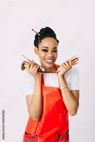 Beautiful young African American beautician woman holding set of make up brushes and eye-shadows