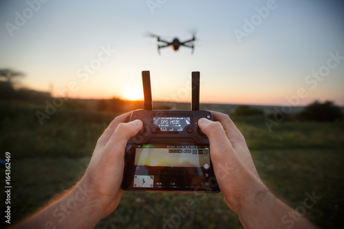 Point of view shot of man holding remote controller with his hands and taking aerial photo video. Quadcopter is flying on background. POV - drone hovers in front of the pilot on suset photo