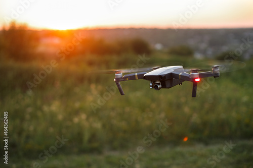 Small compact quadcopter flies in the air on sunset. Drone hovers and stays stable. photo