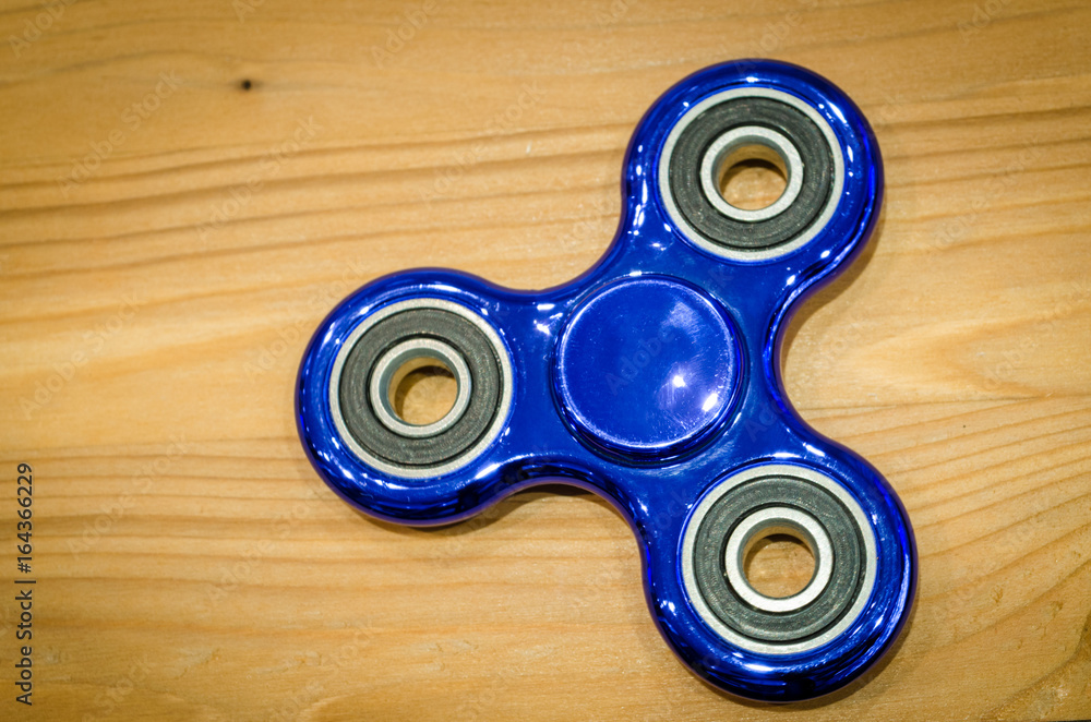 Blue fidget SPINNER stress relieving toy on wood background. Blue fidget SPINNER stress relieving toy on wood background.
