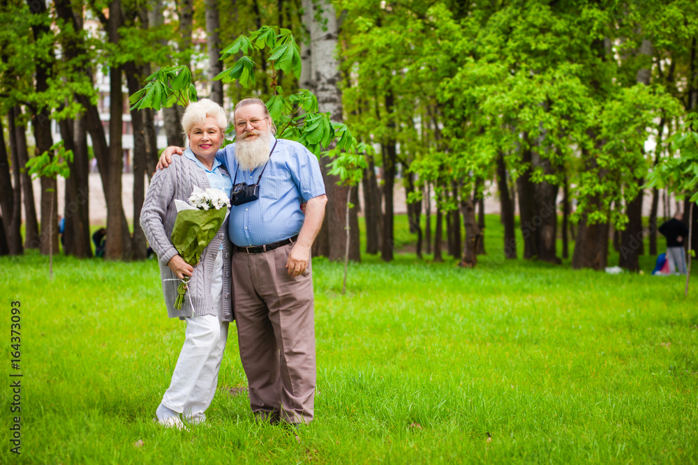 An elderly couple in love stands together in a park with flowers An elderly couple in love stands together in a park with flowers