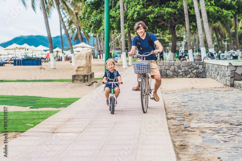 Happy family is riding bikes outdoors and smiling. Father on a bike and son on a balancebike photo