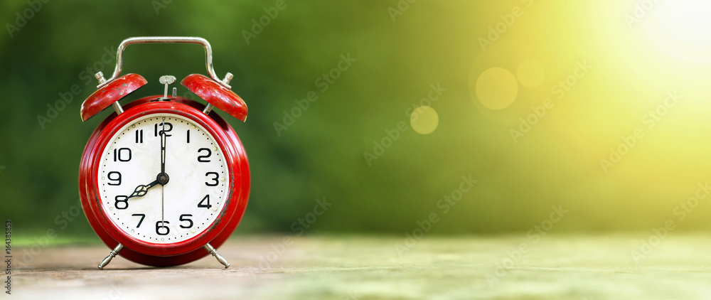 Summertime - web banner of a retro red alarm clock on green background - obrazy, fototapety, plakaty 