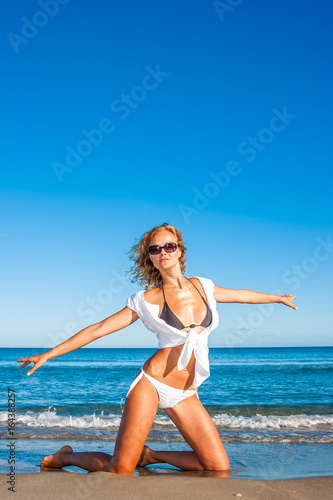fit woman in bikini and white shirt on the beach